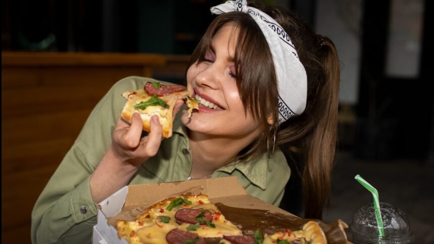 A happy woman enjoying a slice of pizza on her cheat day.